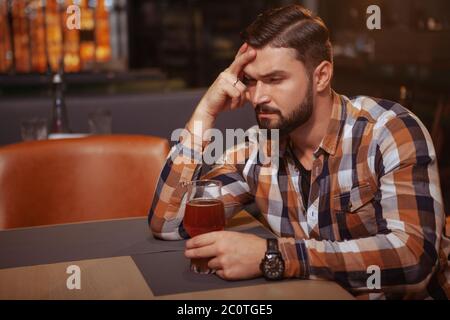 Deprimierter junger Mann, der allein an der Bar trinkt. Ein hübscher Mann, der betrunken aussieht und allein an der Bar mit einem Glas Bier sitzt Stockfoto