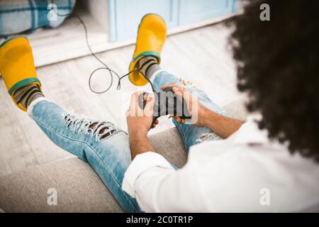 Spieler, der Videospiele spielt. Selektive Fokussierung auf männliche Hände, die Tasten am Joystick drücken, um die auf dem Sofa sitzende Spielstation zu nutzen. Weitwinkelansicht. Schließen Stockfoto
