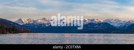 Atemberaubende Panoramasicht auf berühmte Schweizer Alpen Gipfel auf Berner Oberland Eiger Nordwand, Mönch, Jungfrau bei Dämmerung vom Thunersee auf einem sonnigen Stockfoto