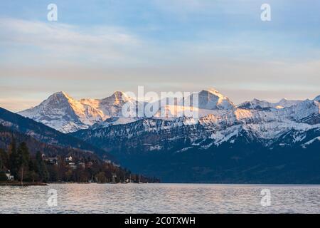 Atemberaubende Panoramasicht auf die berühmten Schweizer Alpen Gipfel im Berner Oberland Eiger Nordwand, Mönch, Jungfrau bei Sonnenuntergang vom Thunersee auf einer Sonne Stockfoto