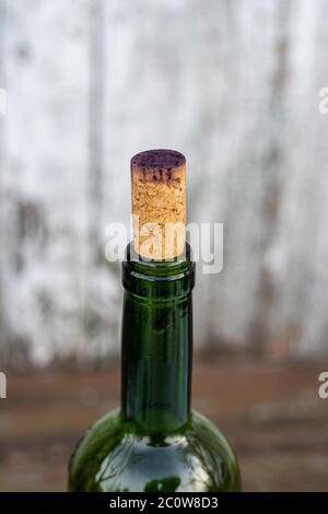 Seitenansicht des Weinengpasses mit Korkkappe, die von dunklem Rotwein gefärbt ist. Transparente grüne Glasflasche Nahaufnahme auf verwackelten Holz Hintergrund Stockfoto