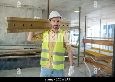 Bauarbeiter in gelber Weste und Handschuhe tragen Holzbrett auf