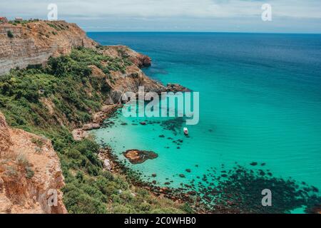 Boot auf azurblauem Meer in der Nähe von Baunty Strand in Alexandra Bucht auf Fiolent. Schöne Aussicht auf die Berge und felsige Küste des azurblauen Schwarzen Meeres, Kap Fiolent, Stockfoto