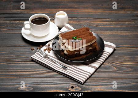 Klassisches Tiramisu Dessert auf Keramikplatte, Milch oder Sahne und Tasse Kaffee auf Holzhintergrund Stockfoto