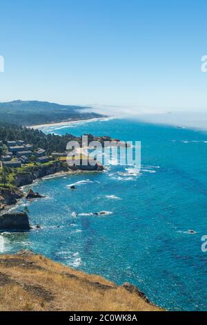 Vertikales Foto - Blick auf die zerklüftete Küste mit Nebel in der Ferne über dem Wasser von Cape Foulweather Overlook in Oregon Stockfoto