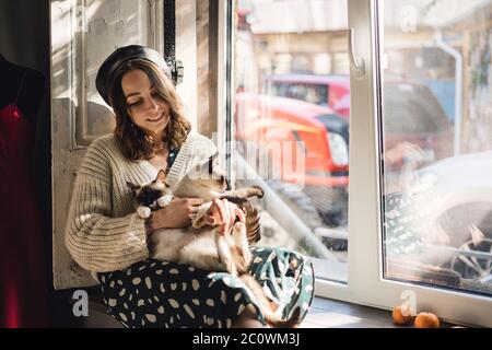 Attraktive Mädchen umarmt ihre Siam Katzen. Indoor-Porträt von niedlichen Frau spielt mit ihren beiden Haustieren. Stockfoto