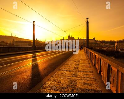 Abenduntergang orange Stimmung auf Manes Brücke mit Silhouette der Prager Burg und Straßenbahn-Trolley Drähte. Prag, Hauptstadt der Tschechischen Republik, Europa. UNESCO-Weltkulturerbe Stockfoto