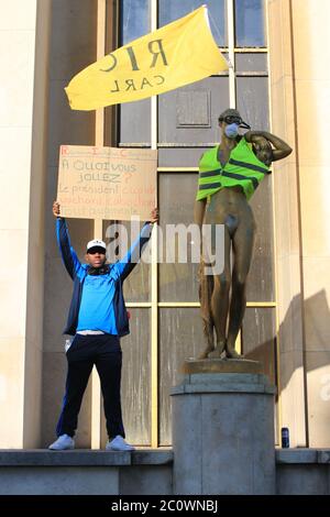 Mann, der einen Karton neben einer goldenen Statue am Trocadero hält, der während der sozialen Proteste in Paris in einer gelben Weste gekleidet war Stockfoto