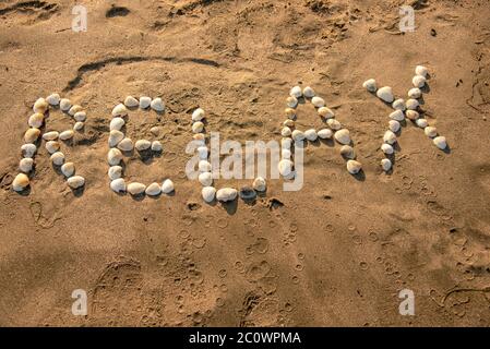 Das Wort Relax ist mit Muscheln auf dem Sand angelegt. Stockfoto