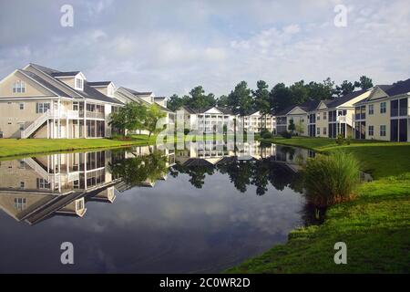 Hintergrund mit einem modernen Viertel mit Gebäuden rund um den Teich. Häuser und Bäume spiegeln sich im ruhigen Wasser während der schönen bewölkten Morgen Stockfoto