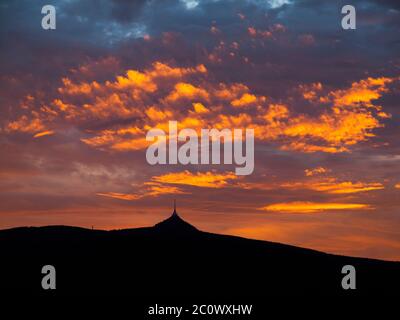 Dramatischer Sonnenuntergang Himmel mit beleuchteten Wolken in den Bergen. Dunkelschwarze Silhouette von Bergrücken und Jested Sender Turm am unteren Rand. Stockfoto