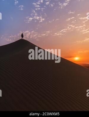 Frau auf der Spitze einer Düne in der Wüste, Wolken, Sonne und Sonnenuntergang Stockfoto