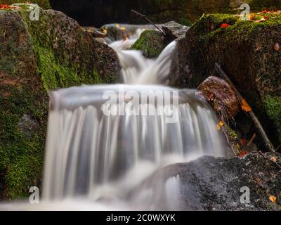 Herbststimmung im Wald mit kleinen Bachwasserfällen. Aufnahme mit langer Belichtung und verschwommenem seidigem Wasserstrahl. Stockfoto