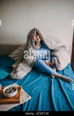 Kaukasische Frau sitzt im Bett am Morgen mit einer Decke bedeckt essen gesunde Getreide Stockfoto
