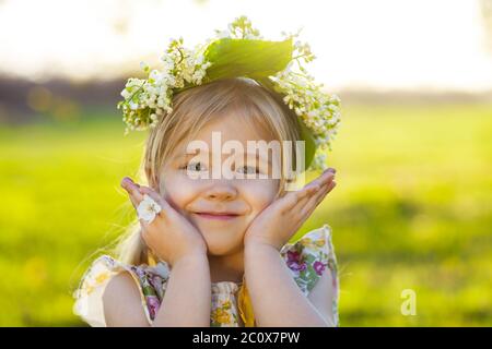 Nettes kleines Mädchen mit blonden Haaren in einem Kranz von Maiglöckchen Stockfoto