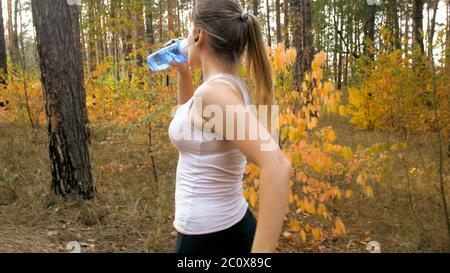 Porträt einer jungen blonden Frau, die im Wald läuft und Wasser aus der Flasche trinkt. Stockfoto