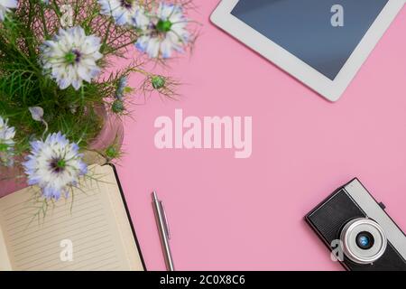 Draufsicht auf Blogger oder Freiberufler Arbeitsbereich mit Tablet, Blumen, Notebook, Stift, Fotokamera auf pastellrosa Hintergrund mit Kopierraum Stockfoto