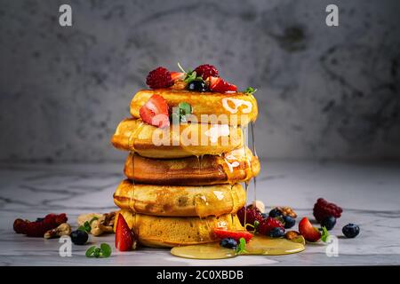 Amerikanische Pfannkuchen mit Beeren und Honig zum Frühstück auf einem hellen Hintergrund dekoriert. Stockfoto