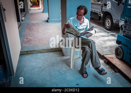 Straßenszene eines Mannes, der eine Zeitung liest, auf einem Plastikstuhl sitzend. Buffalo Road. Little India. Singapur Stockfoto