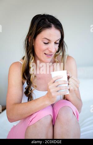 Brünette Frau peering in eine Tasse sitzend auf ihrem Bett Stockfoto