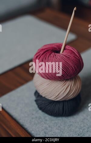 Drei verschieden farbige Kugeln aus DK Garn mit einem Holzhäkelhaken auf einem Holztisch, flacher Fokus. Stockfoto