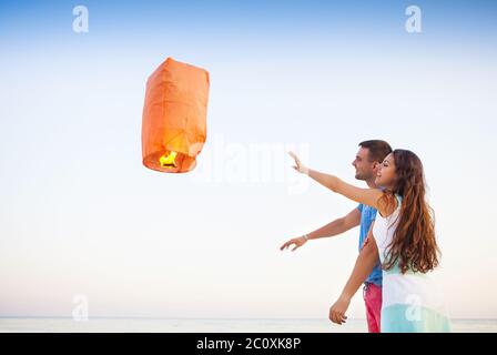 In der Abenddämmerung beginnt ein junges Paar eine rote chinesische Himmelslaterne Stockfoto