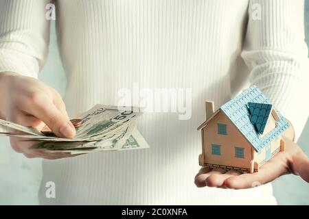 Immobilienpreis und Baukonzept. Mädchen wiegt Geld und ein Spielzeughaus in ihren Händen. Stockfoto
