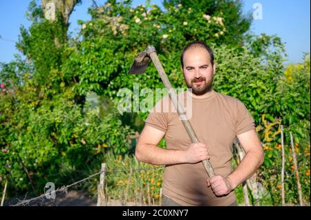 Ein erwachsener Bauer mit einer Hacke, die auf dem Hof posiert. Hochwertige Fotos Stockfoto