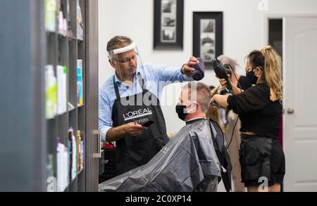 Brantford, Kanada. Juni 2020. Ein Barbier (L) mit Schutzschild schneidet einem Kunden am 12. Juni 2020 in einem Friseursalon der Lynden Park Mall in Brantford, Ontario, Kanada, die Haare. Die Provinz Ontario erlaubte den meisten Regionen außerhalb der Toronto und Hamilton-Gebiete, am Freitag während des COVID-19-Ausbruchs weitere Geschäfte wieder zu eröffnen, einschließlich Restaurantterrassen, Friseursalons und Einkaufszentren. Quelle: Zou Zheng/Xinhua/Alamy Live News Stockfoto