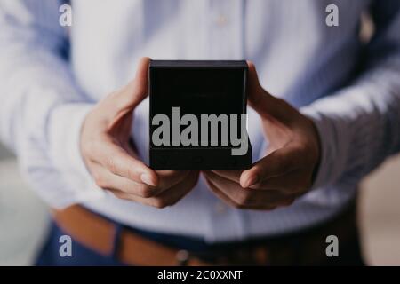 Nahaufnahme des Geschenks auf männlichen Händen. Mann in blauem Hemd. Nicht erkennbarer Mann mit Öffnung schwarze Geschenk-Box. Special Day und festliche Event-Konzept. 2 Mann Stockfoto