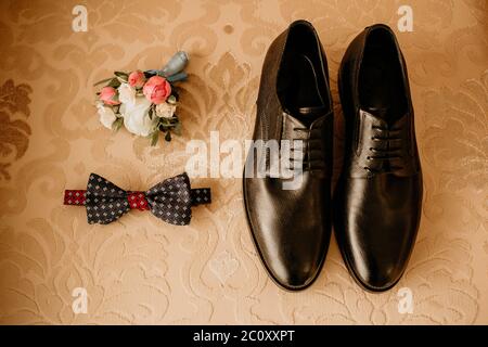 Nahaufnahme von modernen Bräutigam Accessoires. Schwarze Fliege, Lederschuhe und Blumenboutonniere auf rustikalem Hintergrund. Set für formelle Stil des Trageens Stockfoto