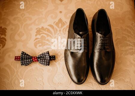 Nahaufnahme von modernen Bräutigam Accessoires. Schwarze Fliege, Lederschuhe und Blumenboutonniere auf rustikalem Hintergrund. Set für formelle Stil des Trageens Stockfoto