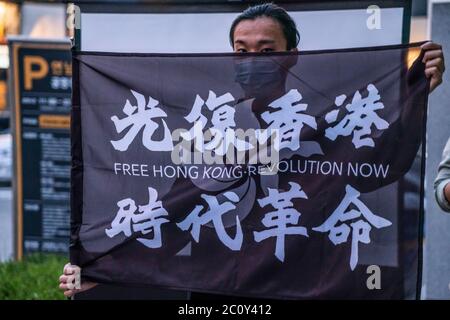 Seoul, Südkorea. Juni 2020. Ein Protestler mit Schutzmaske hält während der Demonstration eine Flagge der Freien Hongkong, Revolution Jetzt. Anlässlich des 1. Jahrestages der Proteste gegen Chinas Sicherheitsgesetze veranstalteten die Menschen in Seoul, Südkorea, eine Protestveranstaltung und eine Videovorführung. Kredit: SOPA Images Limited/Alamy Live Nachrichten Stockfoto