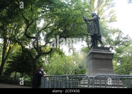 11. Juni 2020, New York, New York, USA: Dieser NYPD-Offizier überwacht die Statue von Christopher Columbus, eingerahmt von Toren, in der Mitte eines platzes im Central Park. Das Denkmal, das letzte Woche markiert und seitdem gereinigt wurde, steht Tag und Nacht unter Beobachtung, wie ein anderes, das über dem Columbus Circle in New York thront. Fragen über die Entfernung von Statuen, die dem italienischen Forscher gewidmet sind, haben sich angesichts des Schadens, den sie den Ureinwohnern zugefügt haben, vermehrt, während einige konföderierte Figuren entfernt wurden. Eine Statue von Columbus wurde heruntergezogen und in einen See in Richmond, VA geworfen, und einer wurde enthauptet Stockfoto