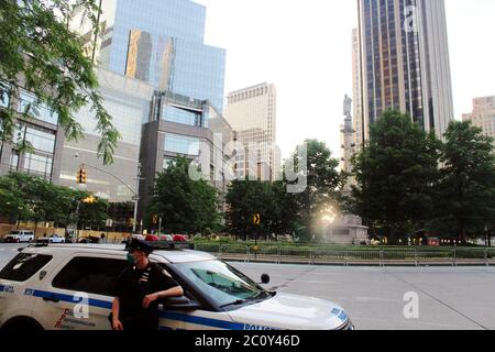 11. Juni 2020, New York, New York, USA: Dieser NYPD-Offizier überwacht die Statue von Christoph Kolumbus, die über dem Columbus Circle in New York thront. Der 75 Meter hohe Midtown-Monolith ist von Toren eingerahmt und Tag und Nacht von fünfzehn Polizeifahrzeugen umgeben. Ein weiteres Kolumbus-Denkmal wird auch im Central Park beobachtet. Fragen über die Entfernung von Statuen, die dem italienischen Forscher gewidmet sind, haben sich angesichts des Schadens, den sie den Ureinwohnern zugefügt haben, vermehrt, während einige konföderierte Figuren entfernt wurden. Eine Statue von Columbus wurde heruntergezogen und in einen See in Richmond, VA geworfen, und einer wurde enthauptet Stockfoto