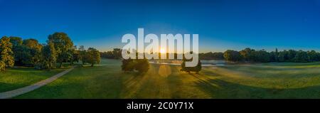 Wunderbares Panorama des Englischen Gartens in München, bayern, deutschland. Früher Nebel steigt, während die Sonne durch zwei grüne Bäume scheint. Mystik Stockfoto