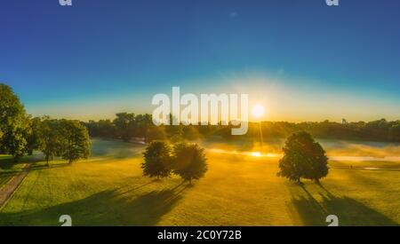 Die Sonne scheint über dem Münchener Enlish-Garten, früh am Morgen fallen Sonnenstrahlen durch die Bäume. Stockfoto