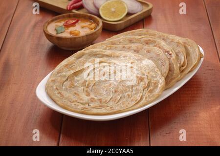 Hausgemachtes Kerala Parotta/Porotta/Paratha/geschichtetes Flachbrot mit Weizen, beliebt in Südindien, serviert in einem Holzbrett mit braunem Holzhintergrund Stockfoto