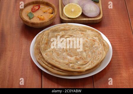 Hausgemachtes Kerala Parotta/Porotta/Paratha/geschichtetes Flachbrot mit Weizen, beliebt in Südindien, serviert in einem Holzbrett mit braunem Holzhintergrund Stockfoto