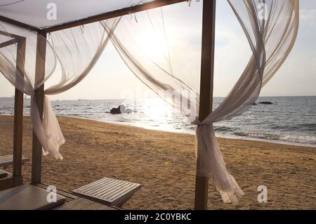 Blick auf den Strand bei Sonnenuntergang durch die Vorhänge eines Strandbettes Stockfoto