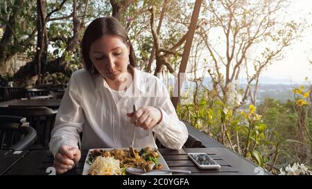 Brunette Frau hat Abendessen Nudeln mit Gemüse in einem Café auf dem Hügel. Stockfoto