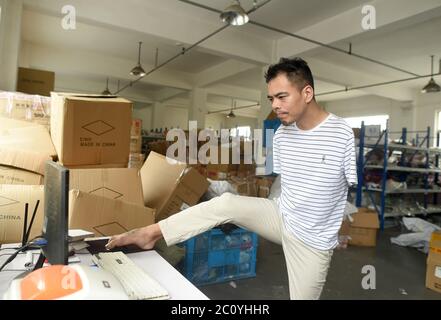 (200613) -- PEKING, 13. Juni 2020 (Xinhua) -- Jin Jiangwei steuert mit dem Fuß eine Maus, um den Beleg seines Online-Shops in Zhuji, Ostchinas Provinz Zhejiang, am 12. Juni 2020 zu drucken. Jin Jiangwei, ein 34-jähriger Dorfbewohner des Dorfes Leshan in der Stadt Zhuji, verlor seine Arme aufgrund eines Unfalls im Alter von fünf Jahren. 2016 eröffneten Jin Jiangwei und sein Bruder einen Online-Shop für den Verkauf von Socken, in dem Jin für die Ladenplanung und den Kundenservice zuständig ist. Nach Jahren der Praxis ist Jin in in der Lage, mit seinen Füßen so schnell zu tippen wie normale Menschen. Der Jahresumsatz des Ladens hat eine Milli überschritten Stockfoto