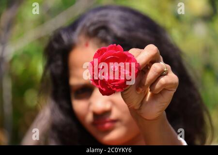 Das verschwommene Gesicht eines jungen Mädchens, das eine rote Rosenblüte in offenen Haaren gibt Stockfoto