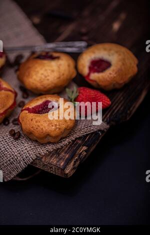 Erdbeermuffin und Kaffeebohnen auf einem Holzbrett auf dunklem Holzhintergrund. Schokoladenmuffins auf dunklem Hintergrund, selektiver Fokus. Stockfoto