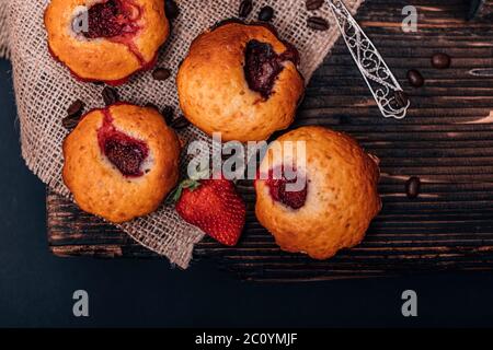 Erdbeermuffin und Kaffeebohnen auf einem Holzbrett auf dunklem Holzhintergrund. Schokoladenmuffins auf dunklem Hintergrund, selektiver Fokus. Stockfoto