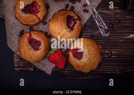 Erdbeermuffin und Kaffeebohnen auf einem Holzbrett auf dunklem Holzhintergrund. Schokoladenmuffins auf dunklem Hintergrund, selektiver Fokus. Stockfoto