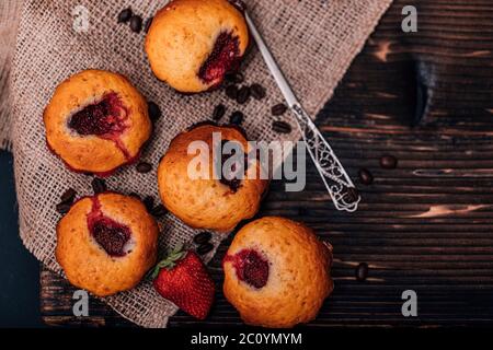 Erdbeermuffin und Kaffeebohnen auf einem Holzbrett auf dunklem Holzhintergrund. Schokoladenmuffins auf dunklem Hintergrund, selektiver Fokus. Stockfoto