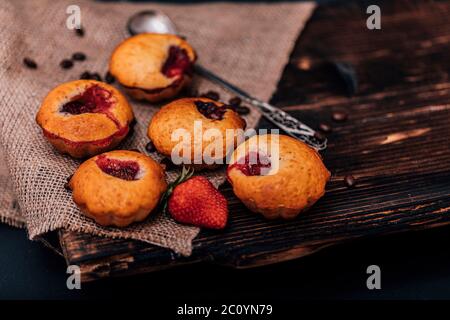 Erdbeermuffin und Kaffeebohnen auf einem Holzbrett auf dunklem Holzhintergrund. Schokoladenmuffins auf dunklem Hintergrund, selektiver Fokus. Stockfoto