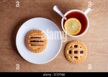 Tasse Tee und Zitrone, Kekse mit Marmelade in Untertasse Tabelle Draufsicht Stockfoto