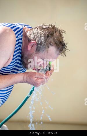 Mann trinkt Wasser aus einem Schlauch an einem heißen Tag Stockfoto